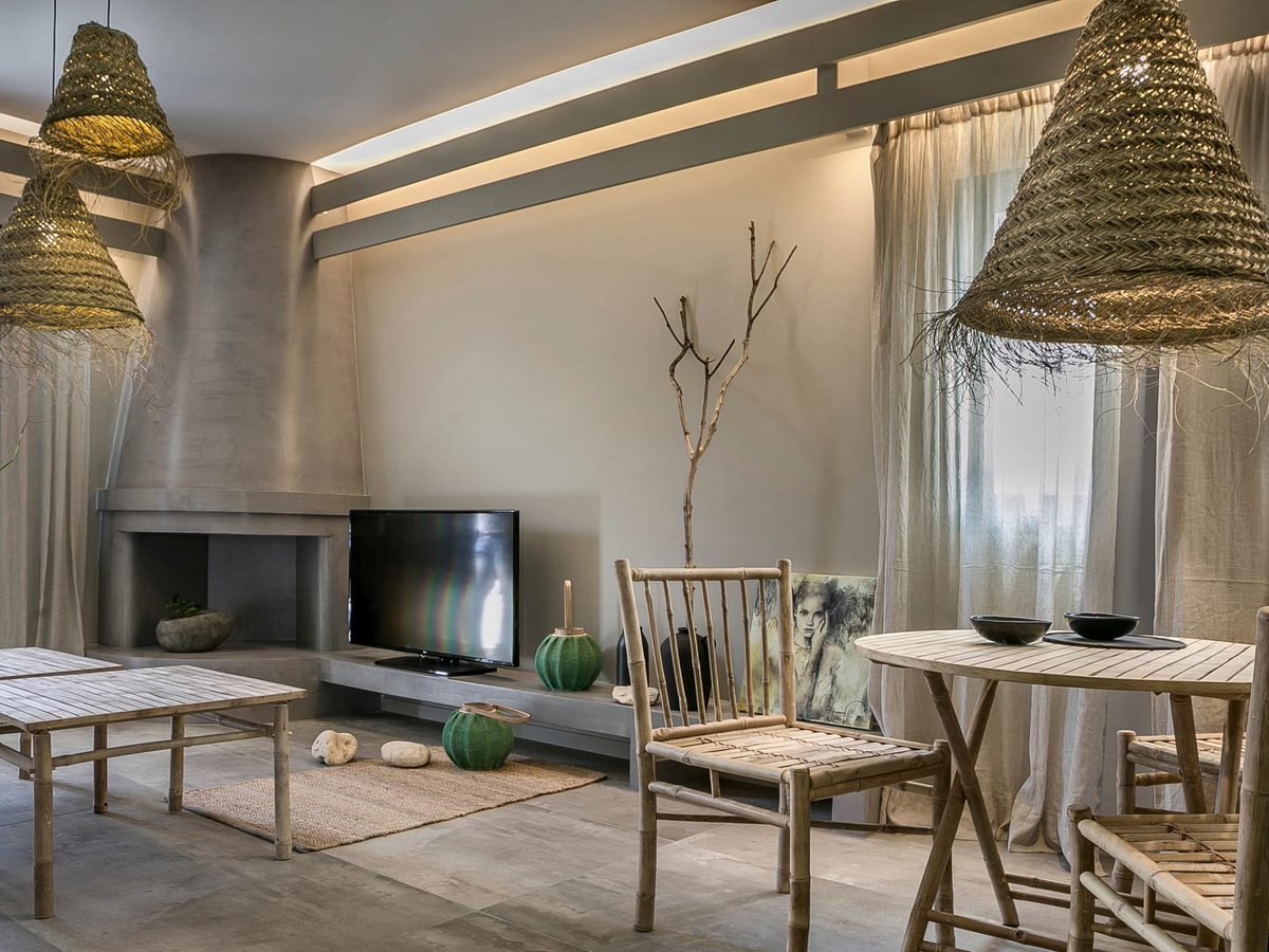 Suite living room with a fireplace and flat-screen TV, rattan chairs, a round dining table and woven pendant lights over a tiled floor.