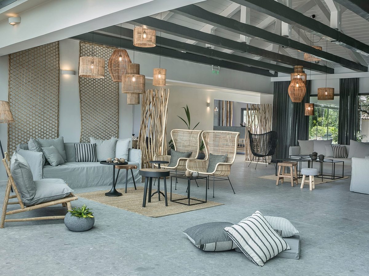 Open-plan lobby lounge with pale sofas, cane armchairs, low coffee tables and rattan pendant lights over a polished grey floor.