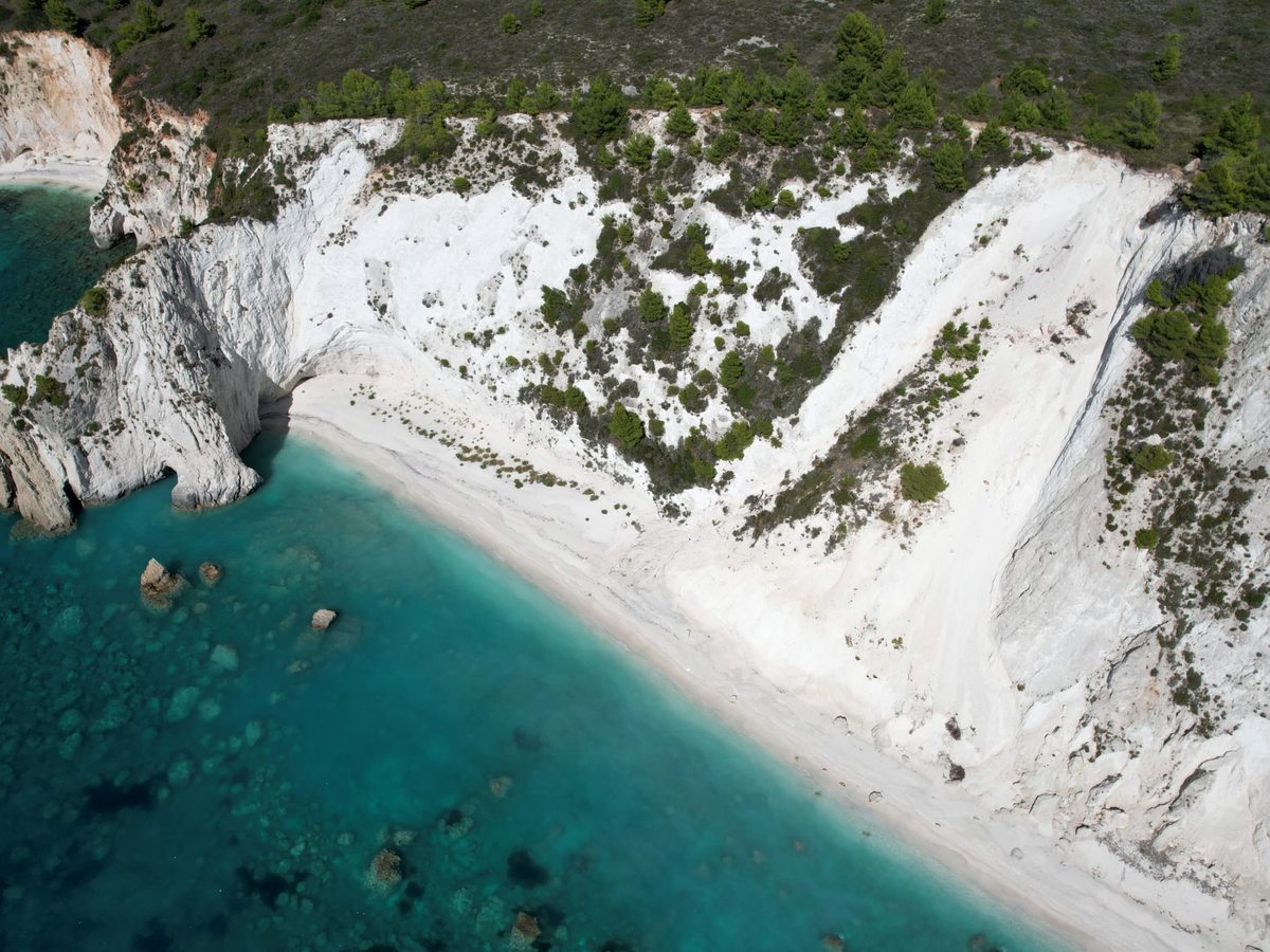 Aerial view of sheer white limestone cliffs dropping to a small pebble cove and clear turquoise sea.