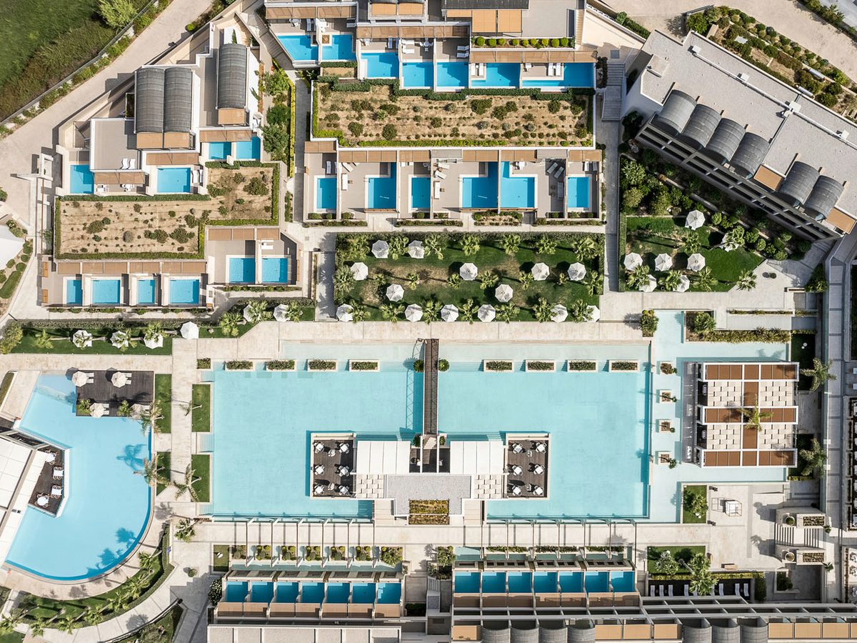 An aerial view of the resort's large rectangular main pool ringed by sun-lounger terraces, with rows of small private plunge pools on the room terraces beyond.