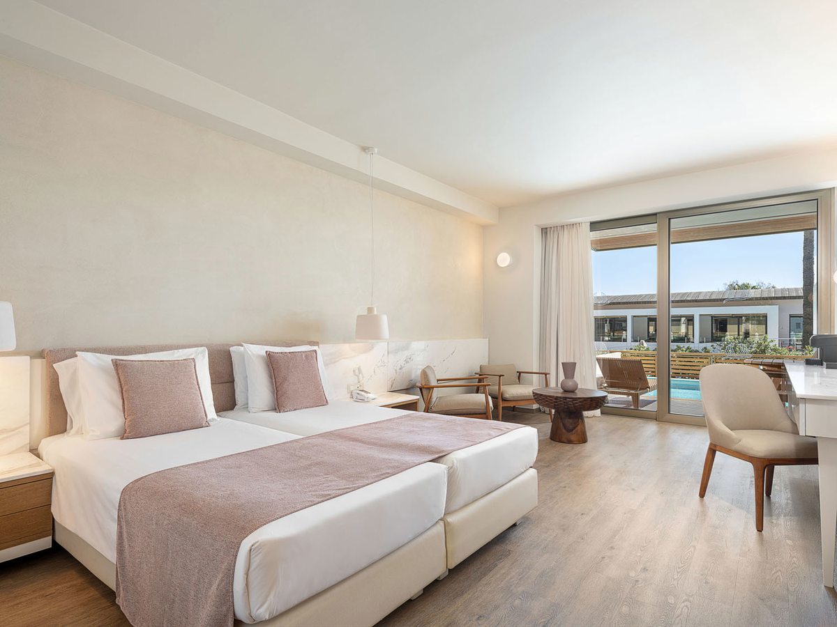 A twin room with two single beds, a desk and armchair, and sliding glass doors to a furnished terrace.