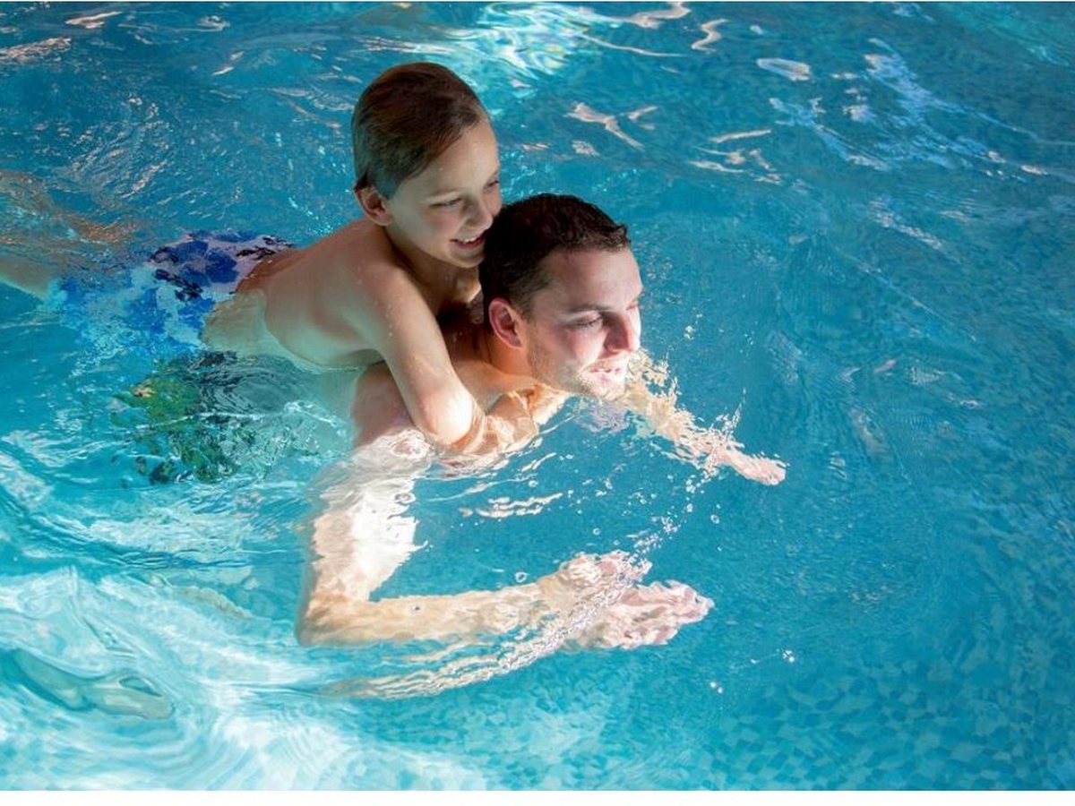 People swimming in a bright indoor pool with clear blue water and a tiled surround.