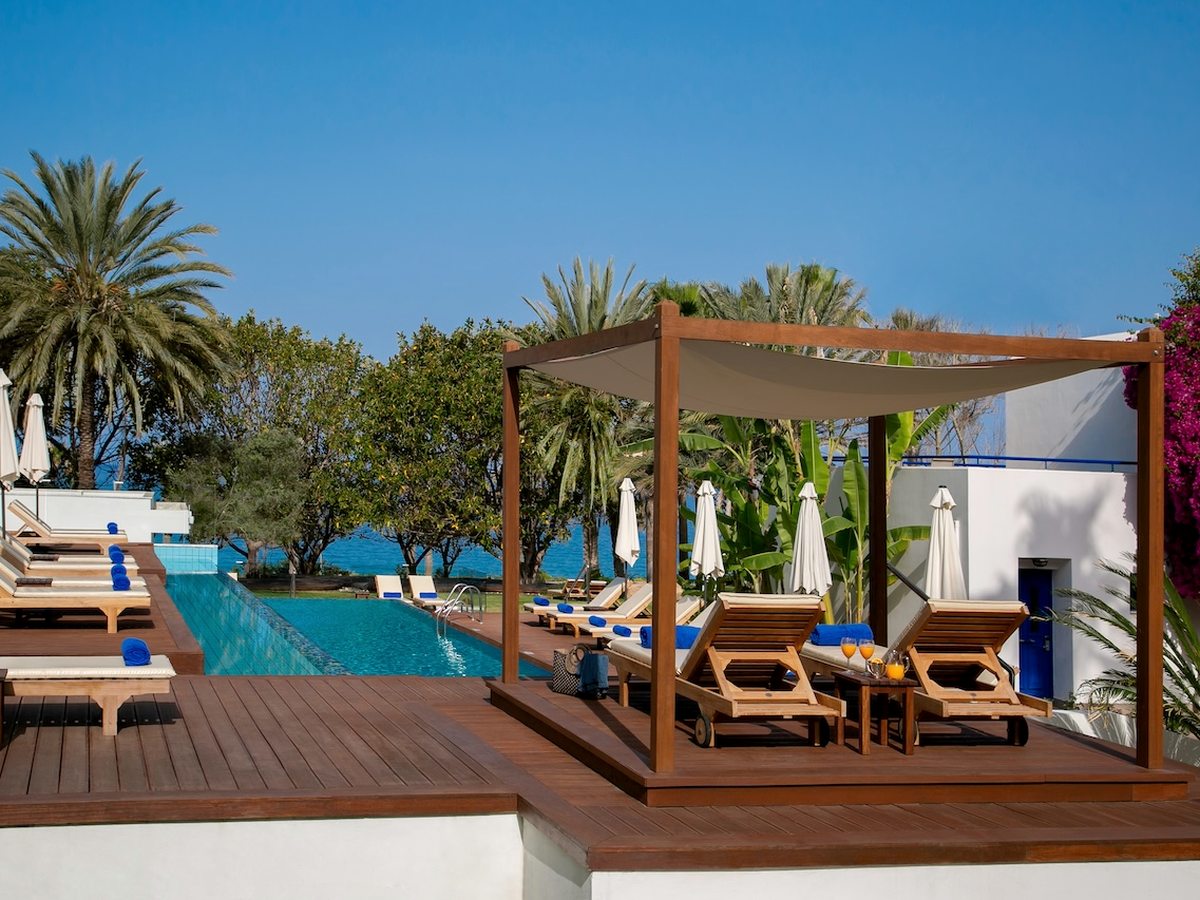 Wooden sunloungers under a pergola shade canopy on a deck beside the pool.