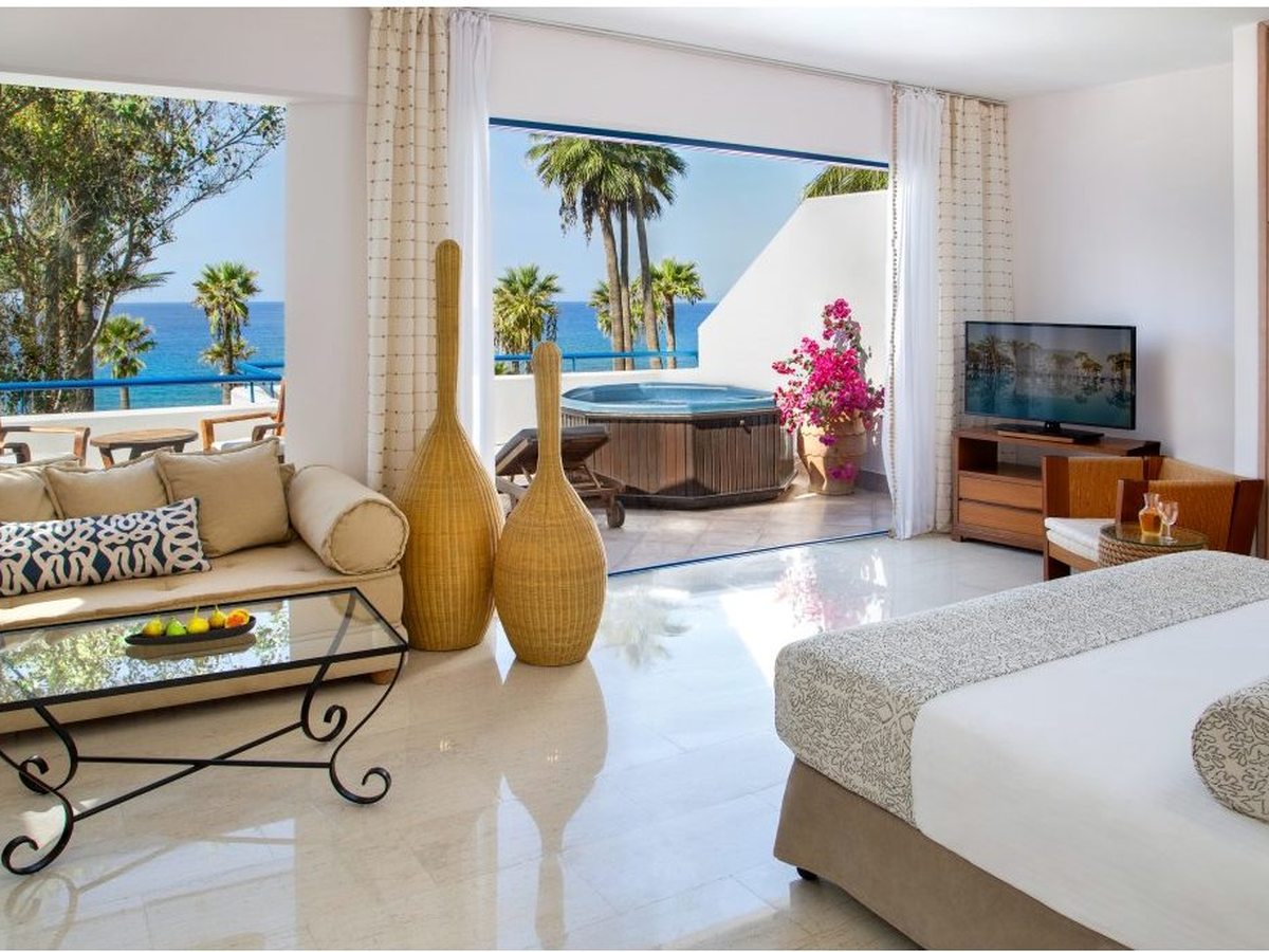 A suite with a double bed, a sofa and a sitting area, and a large window framing the sea.