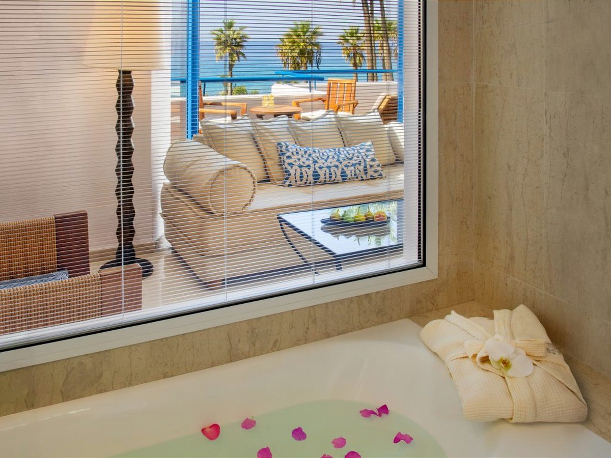 A bathroom with a bathtub set beneath a window that looks through to the room and the sea.
