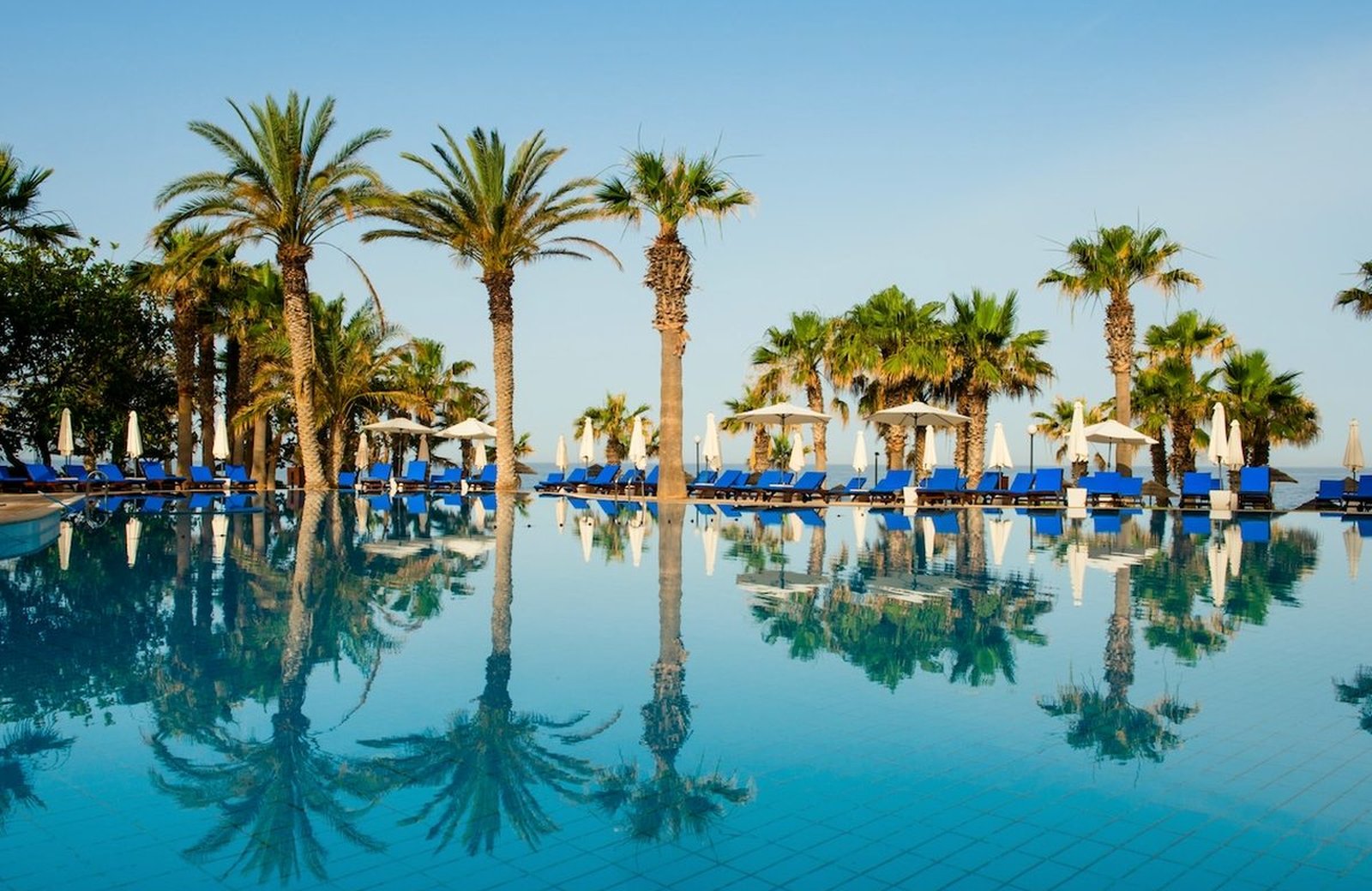 The lagoon pool at Azia Resort & Spa, lined with tall palms and blue loungers, looking west over the water to the sea.
