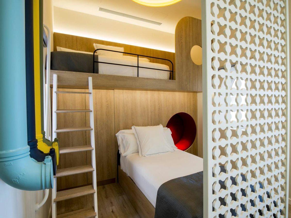 A children's alcove with a bunk bed, a ladder to the top bunk and a red porthole nook, set behind a white lattice screen.