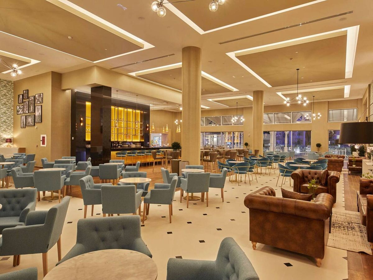 A spacious hotel lobby lounge with pale-blue armchairs, leather sofas and a bar counter at the far end.