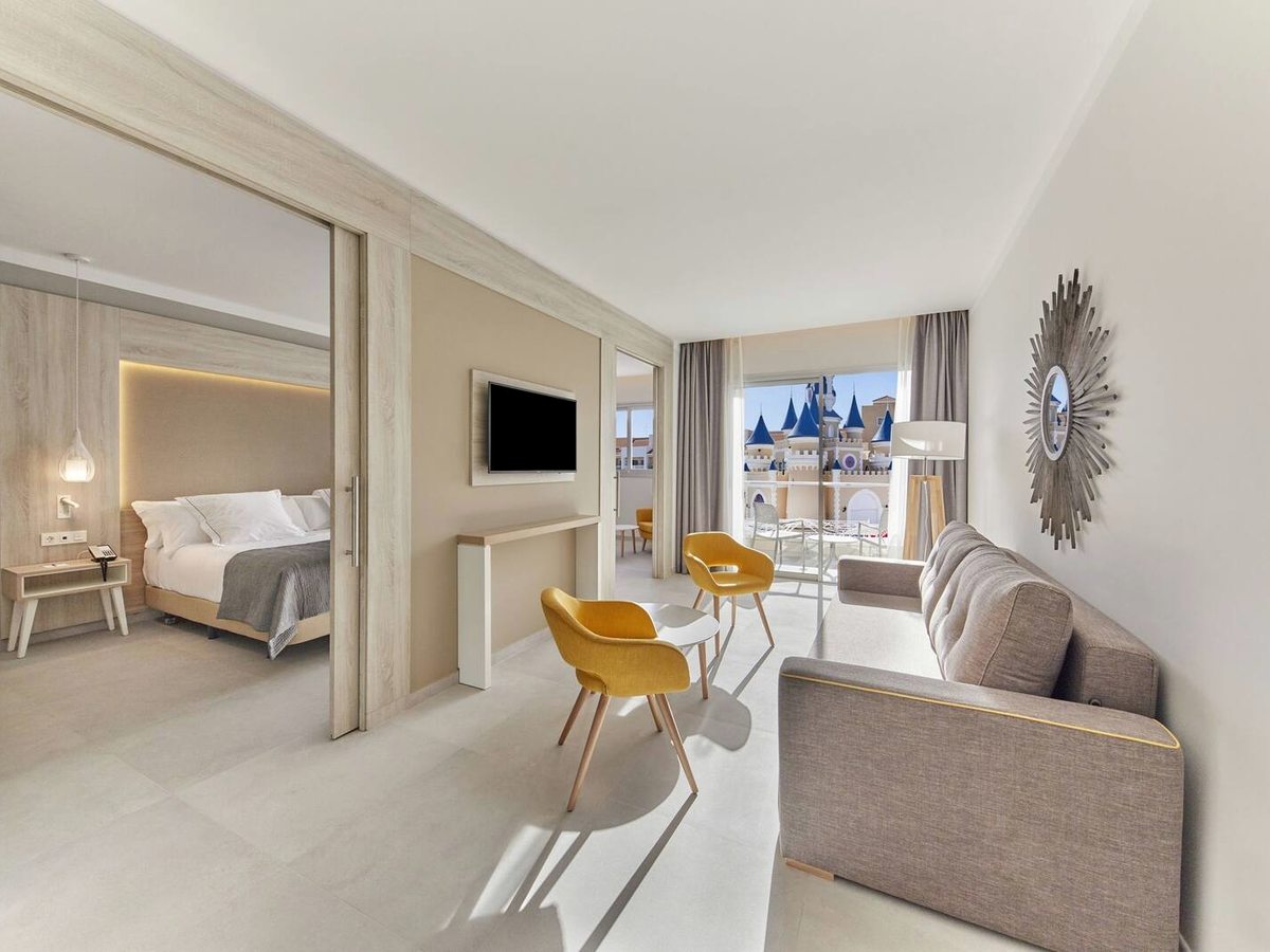 A neutral-toned suite with a sofa and yellow armchairs in the living area and the double bedroom through an open sliding partition.