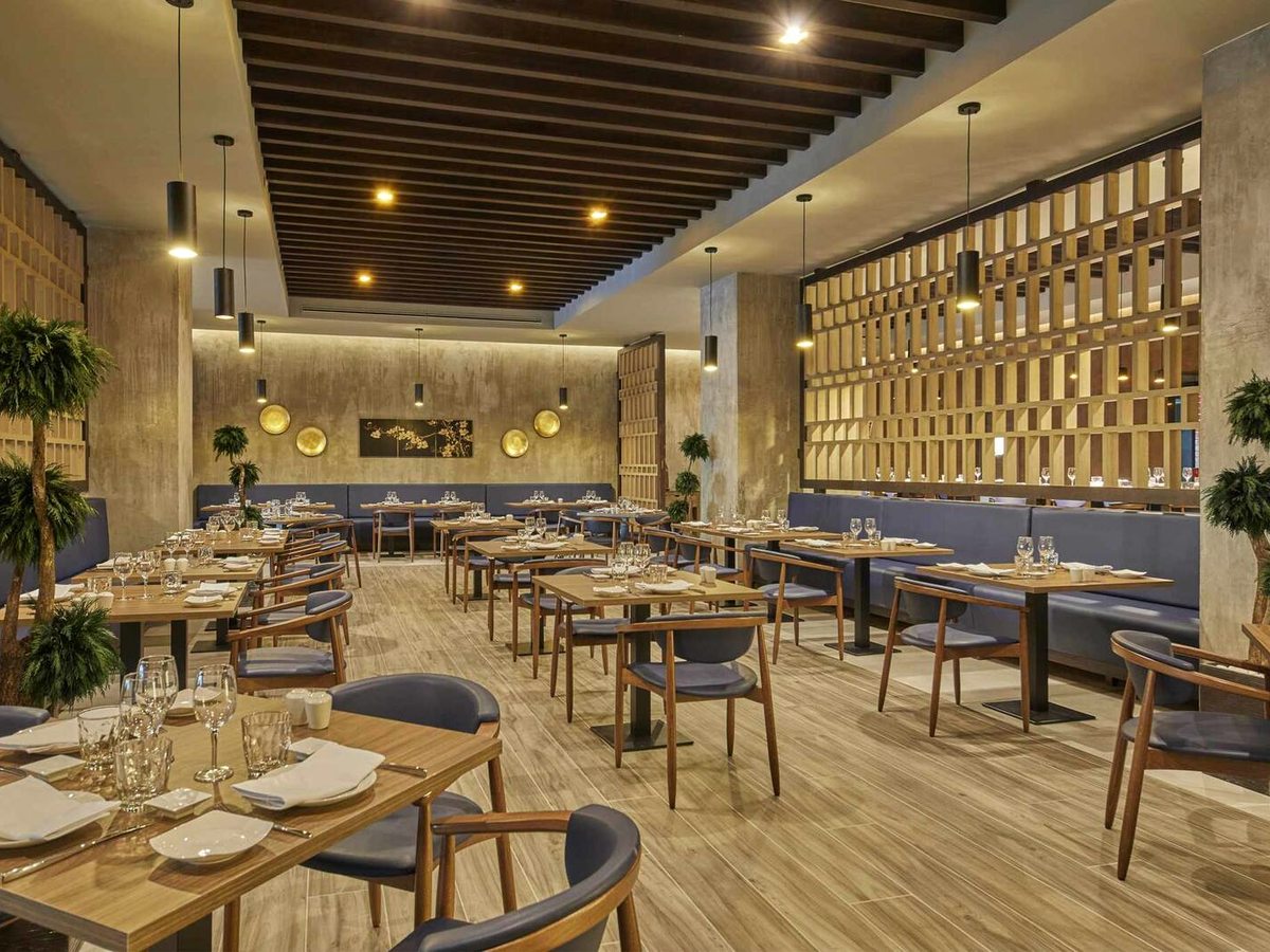 An indoor restaurant dining room with laid tables, blue upholstered chairs and a wood-slatted ceiling.