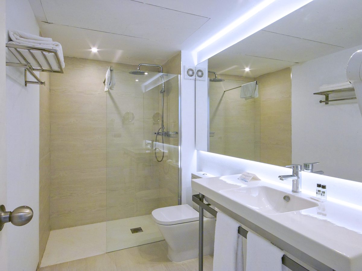 Bright bathroom with a glass-screened walk-in rain shower, a wide basin with a mirror and a wall-mounted hairdryer.