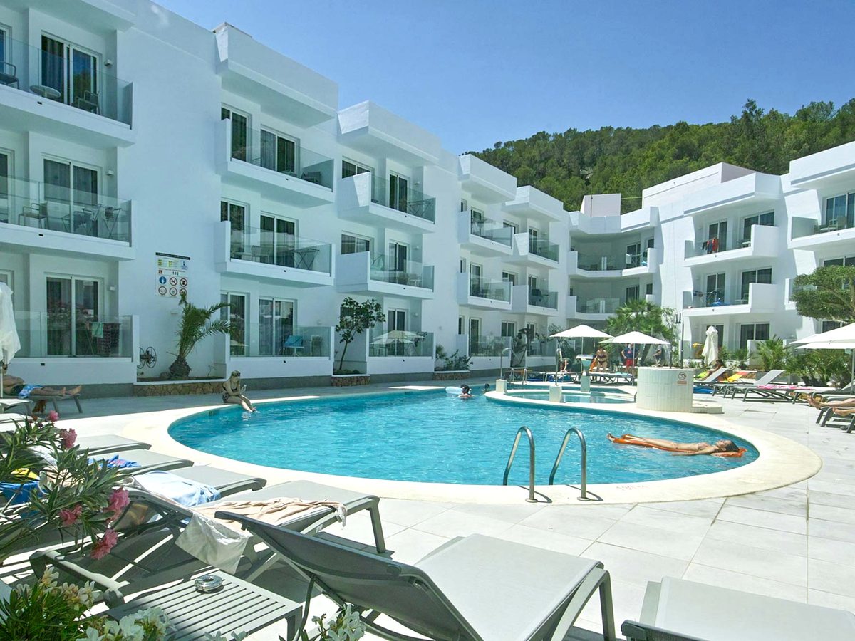 A smaller round freshwater pool with a central water-jet feature, set in a courtyard between white apartment blocks with balconies and edged with sun loungers.