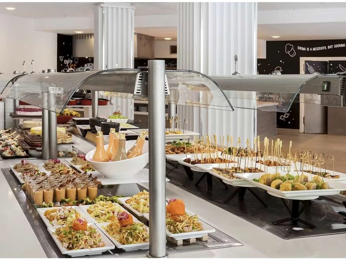 A long white buffet counter under curved glass sneeze-guards, set with trays of canapes, skewers, salads and desserts.