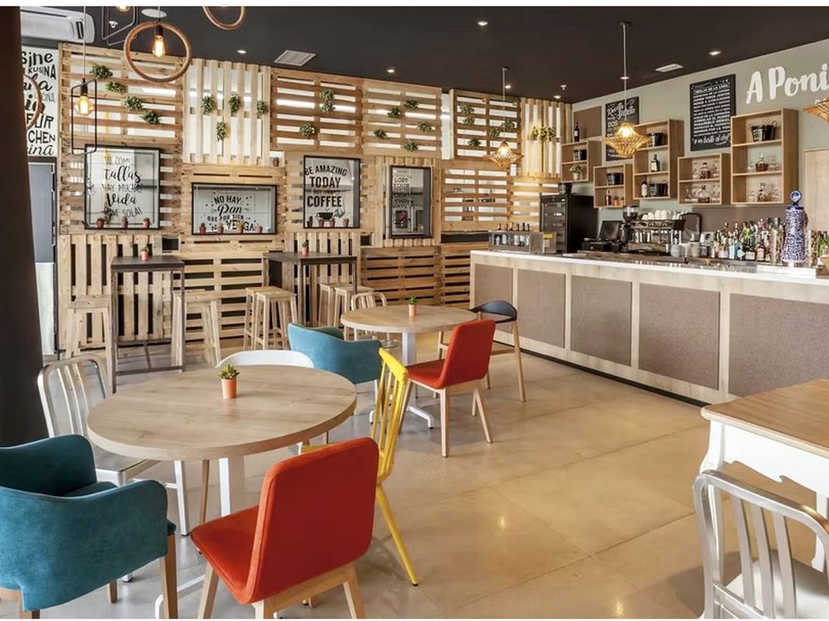 The A Poniente gastrobar interior, with pale-wood pallet-panel walls, colourful tub chairs at round tables, pendant lights and a bar counter with chalkboard menus.