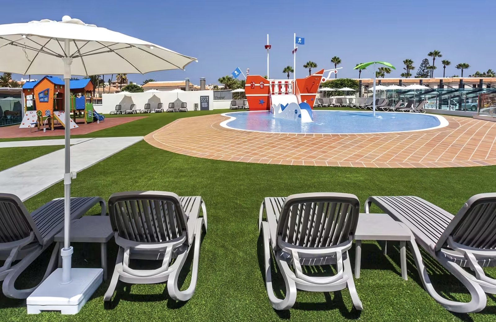 The children's pool, pirate ship splash park and playground on the lawns at Barceló Corralejo Sands, under a clear sky.