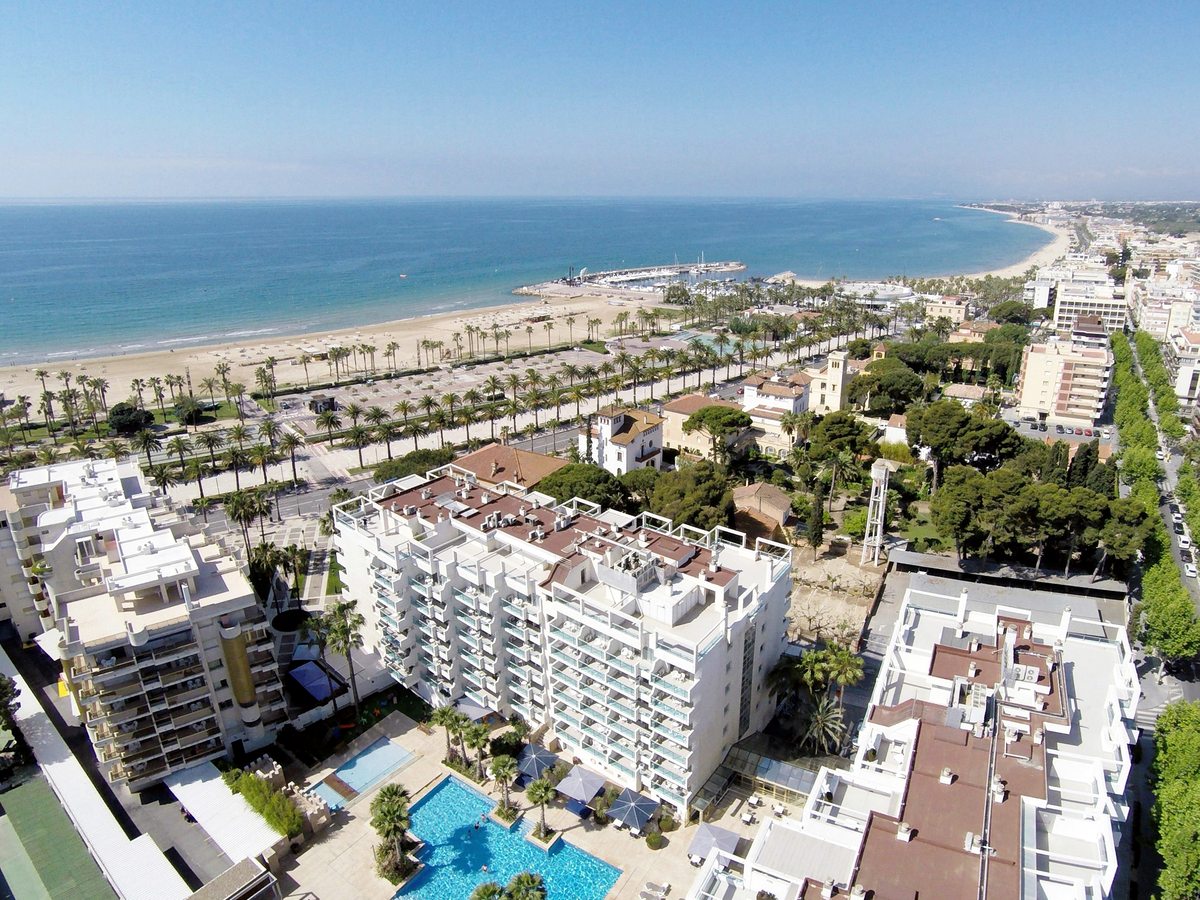 A high aerial of the long curving beach and promenade with the low-rise resort town behind