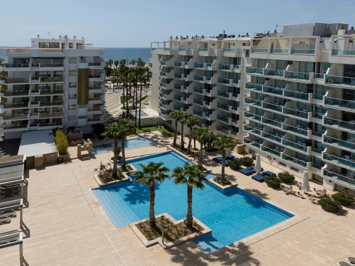 An aerial of a rectangular pool and a smaller pool set in a paved courtyard between the hotel's wings, the sea beyond