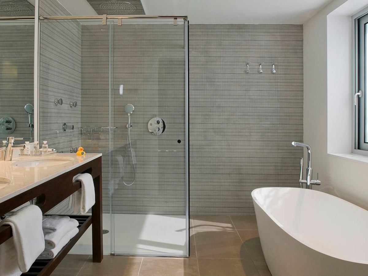 A bathroom with a freestanding oval bath by a window, a glass walk-in shower and a double washbasin