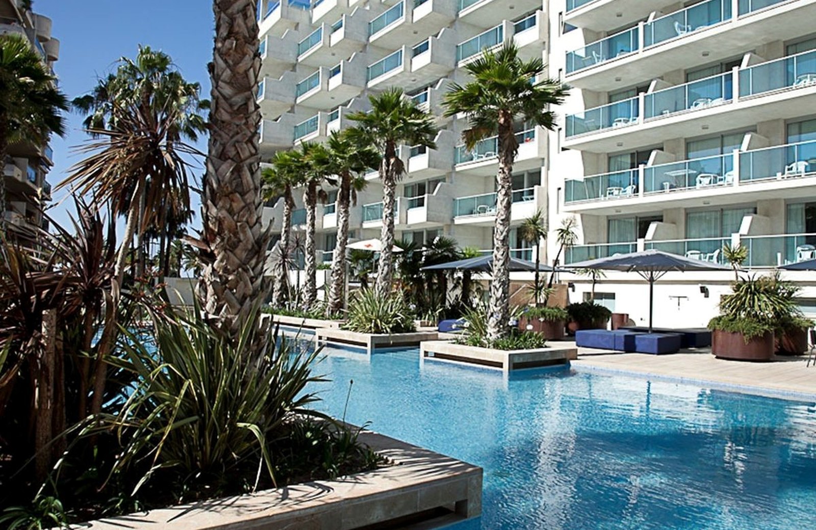 The palm-lined main pool at Blaumar Hotel, below the seafront building's balconies.