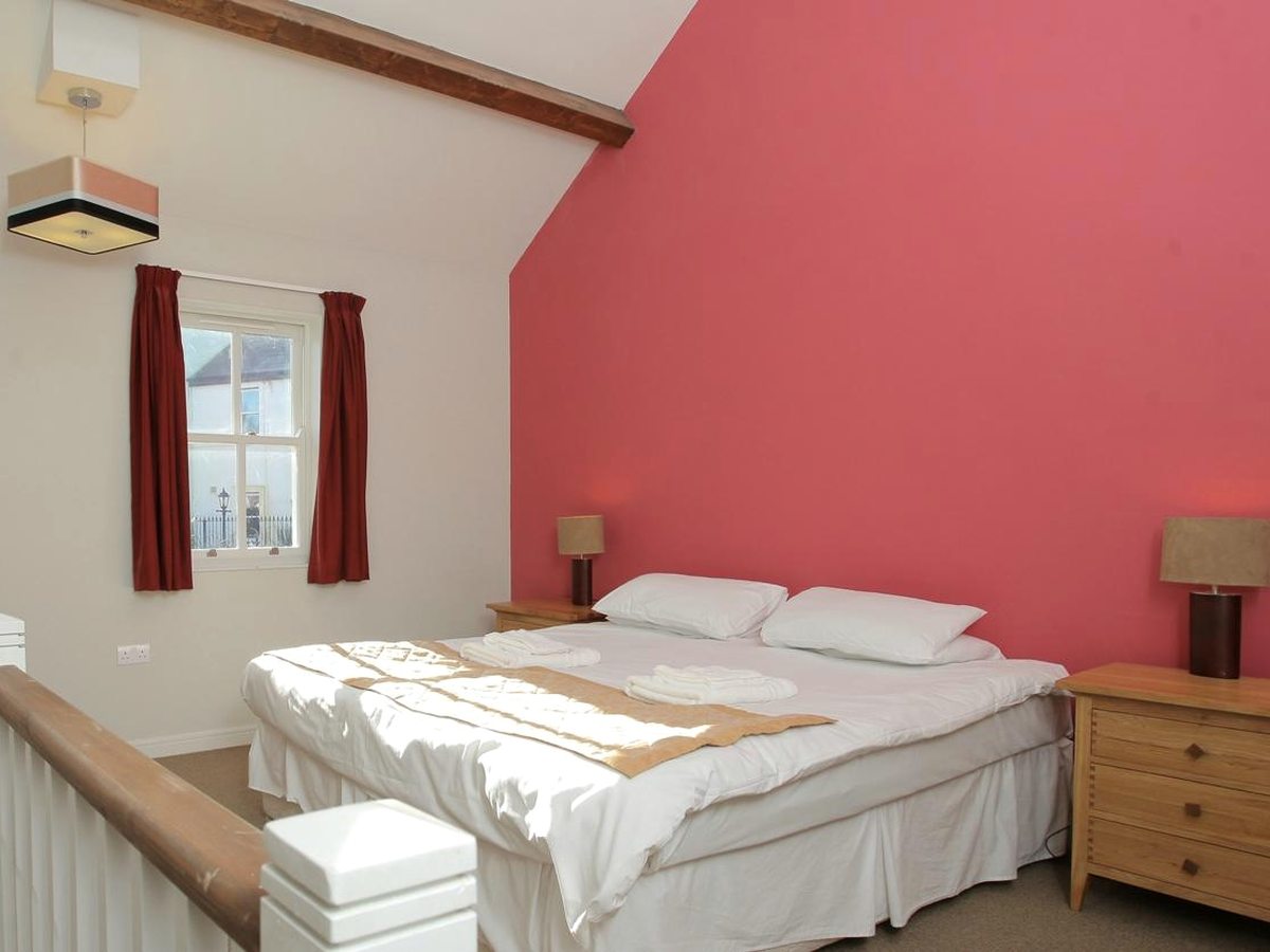 A lodge double bedroom with a white-dressed bed, a red feature wall, bedside tables and lamps and a sloped beamed ceiling.