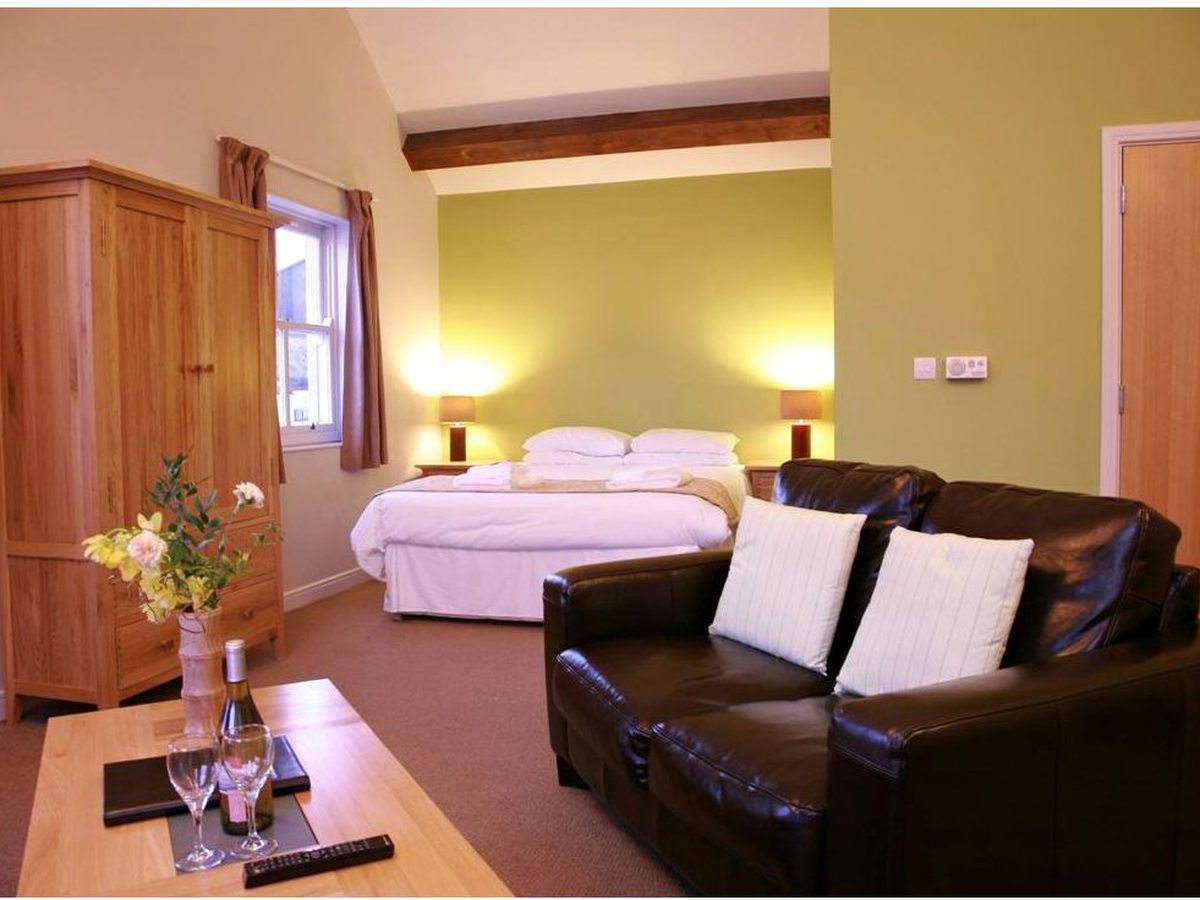 A studio room with a double bed and a leather sofa in one space, an oak wardrobe, a green feature wall and a low coffee table.