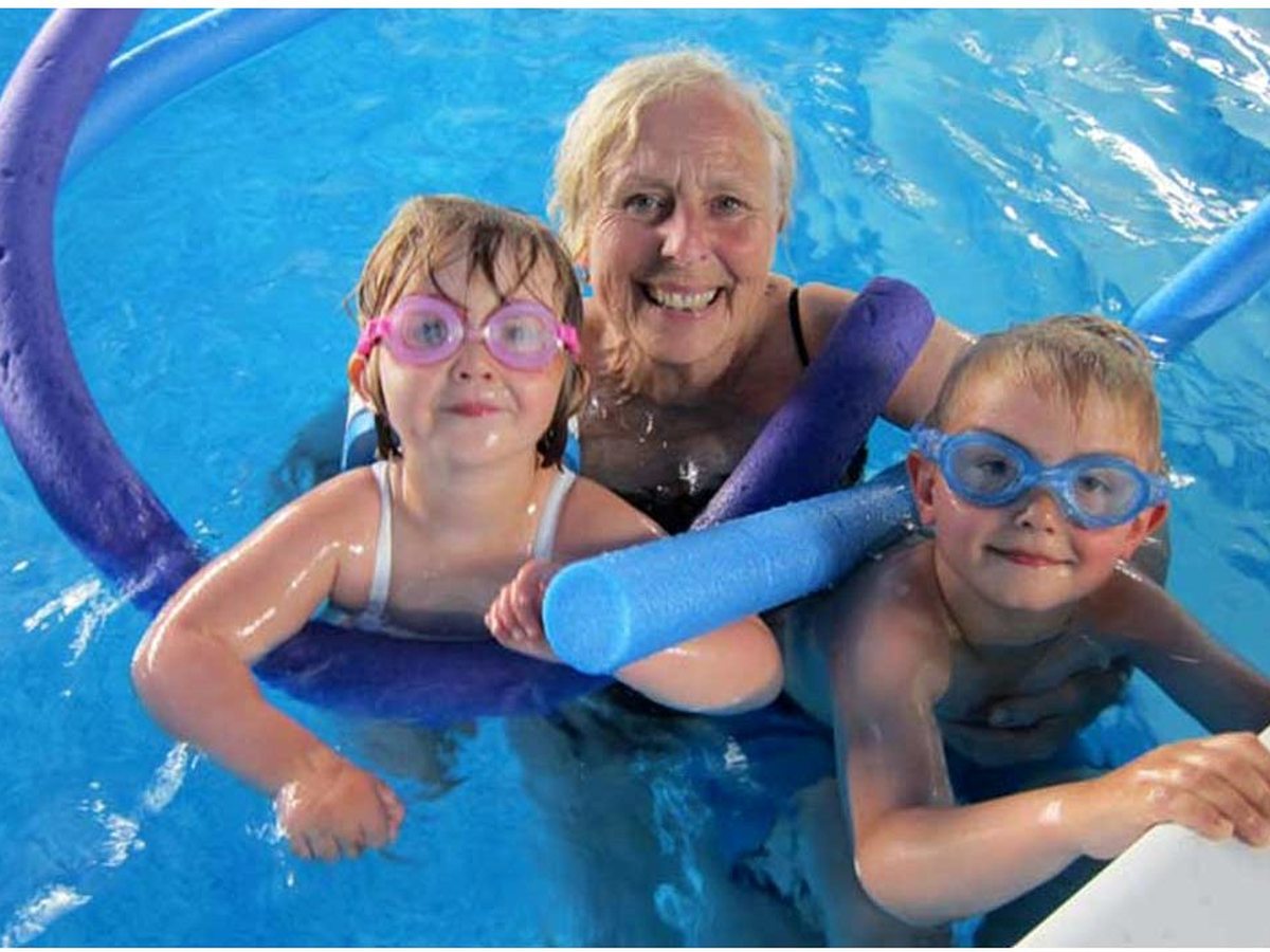 A grandparent and two children in goggles and armbands holding a foam pool noodle in Bosinver's warm indoor pool.