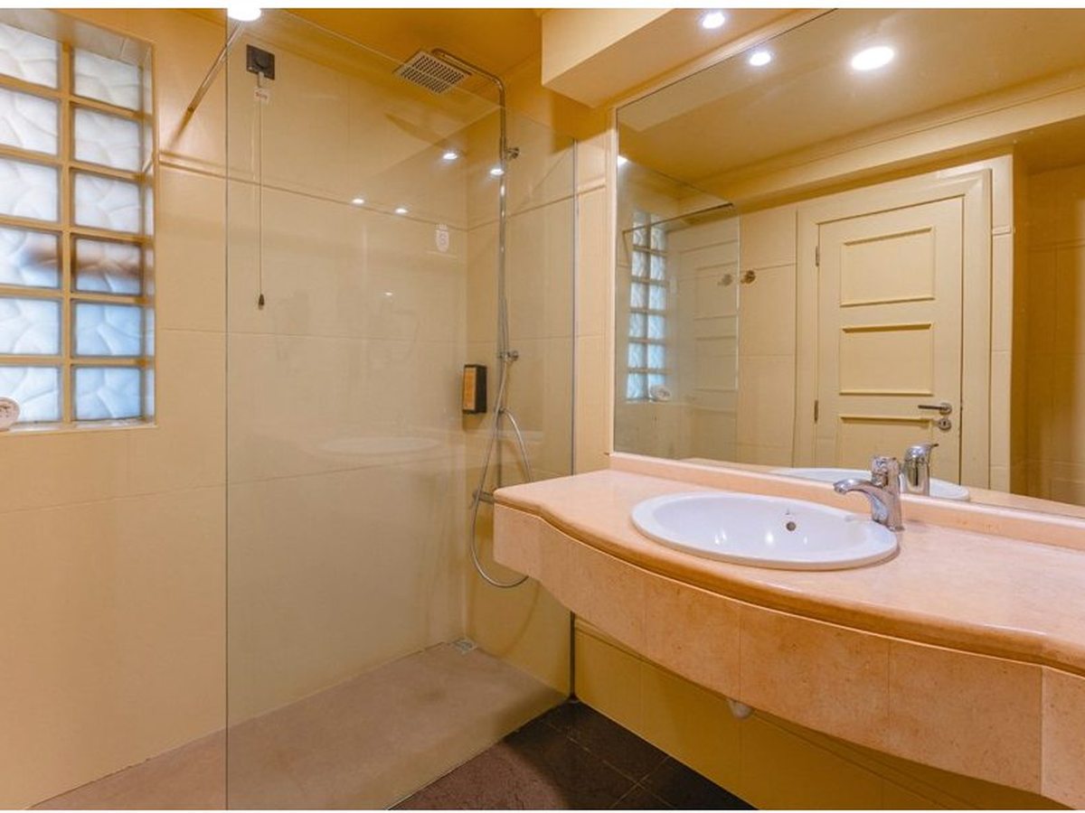 Bathroom with a glass-screened walk-in rainfall shower beside a vanity unit and mirror.