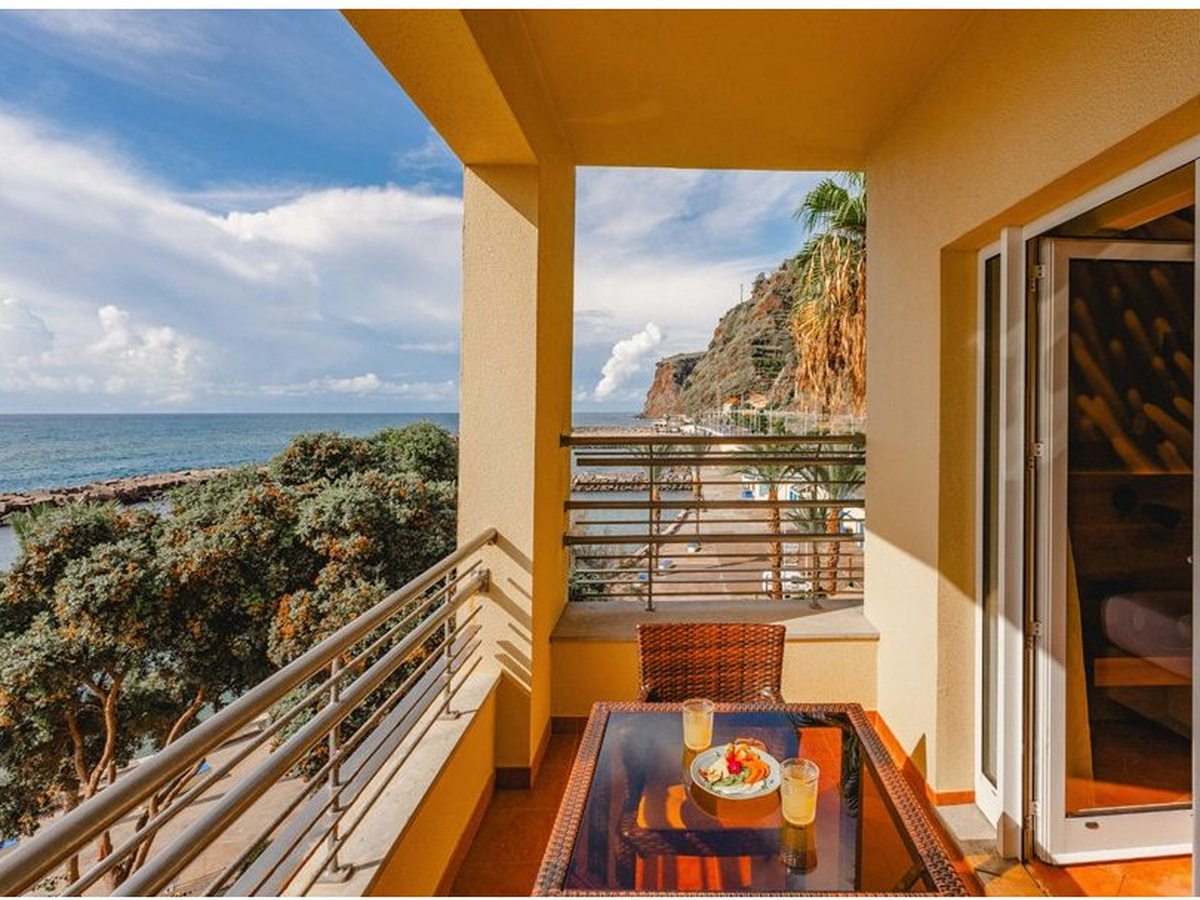 Room balcony with a table and chairs looking out over the sea, a breakwater and a headland.