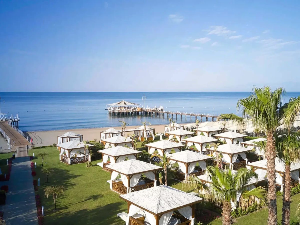 The private sandy beach with white cabanas and parasols on a lawn above the sand, a timber pier running out into a calm sea.