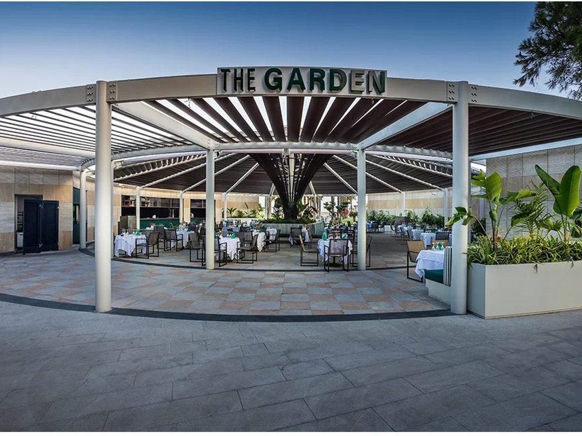 The open-sided circular pavilion of The Garden restaurant, its name in green letters above a louvred canopy over set dining tables.