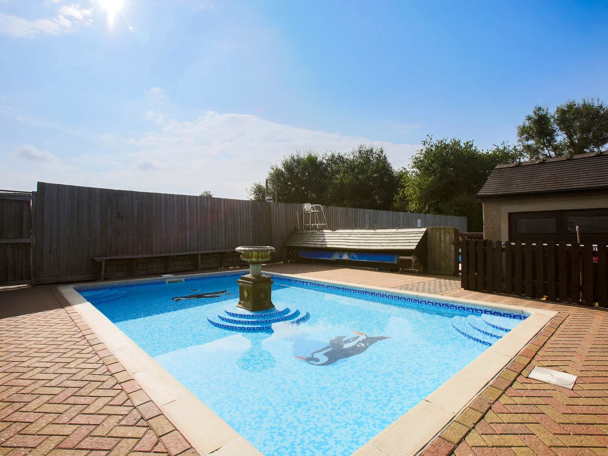 A smaller square pool with a central stone fountain and a dolphin mosaic on the floor, enclosed by fencing.