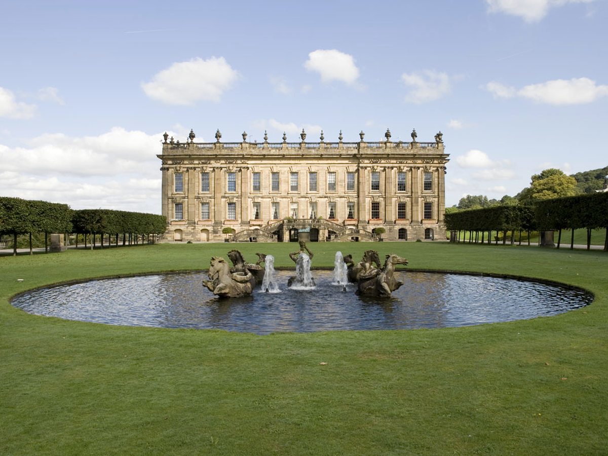 The honey-stone facade of Chatsworth House across its formal garden and fountain pond.