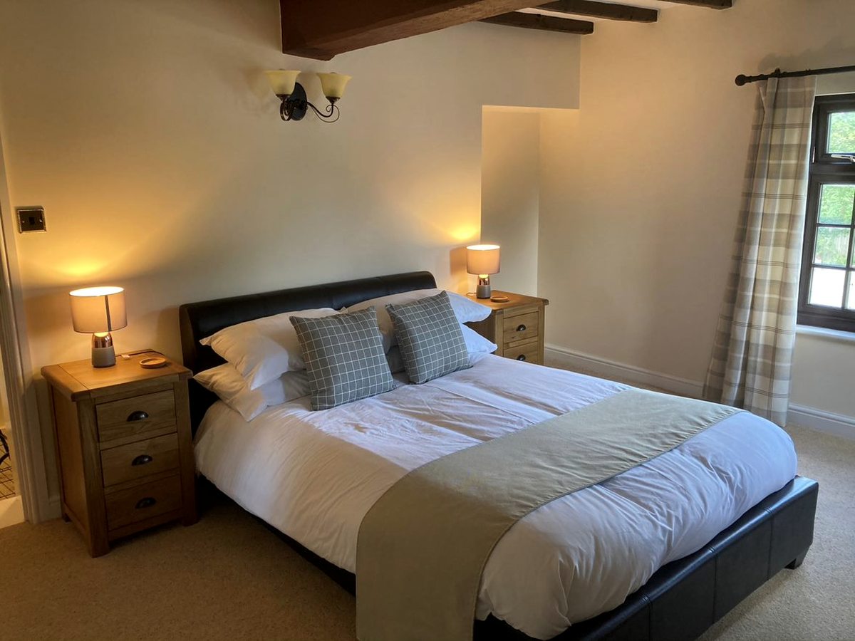 A double bedroom with a dark wooden bed, a green runner and bedside lamps under a sloping ceiling.