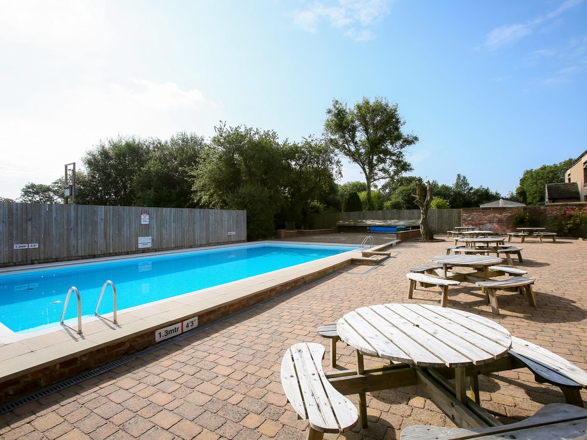 Wooden picnic benches on the paved pool terrace beside the swimming pool.