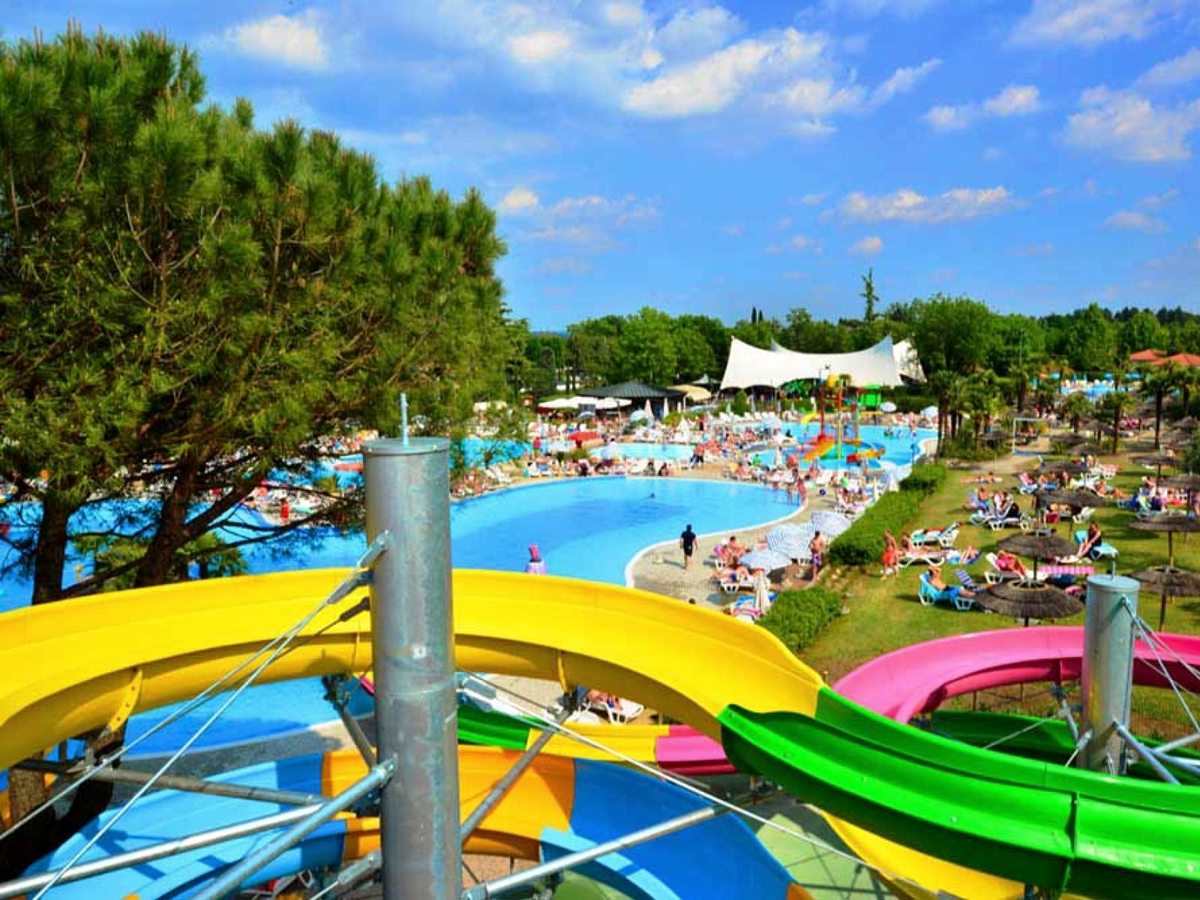 Yellow, green and pink open flume waterslides curving down toward a large freeform pool busy with sunbathers.