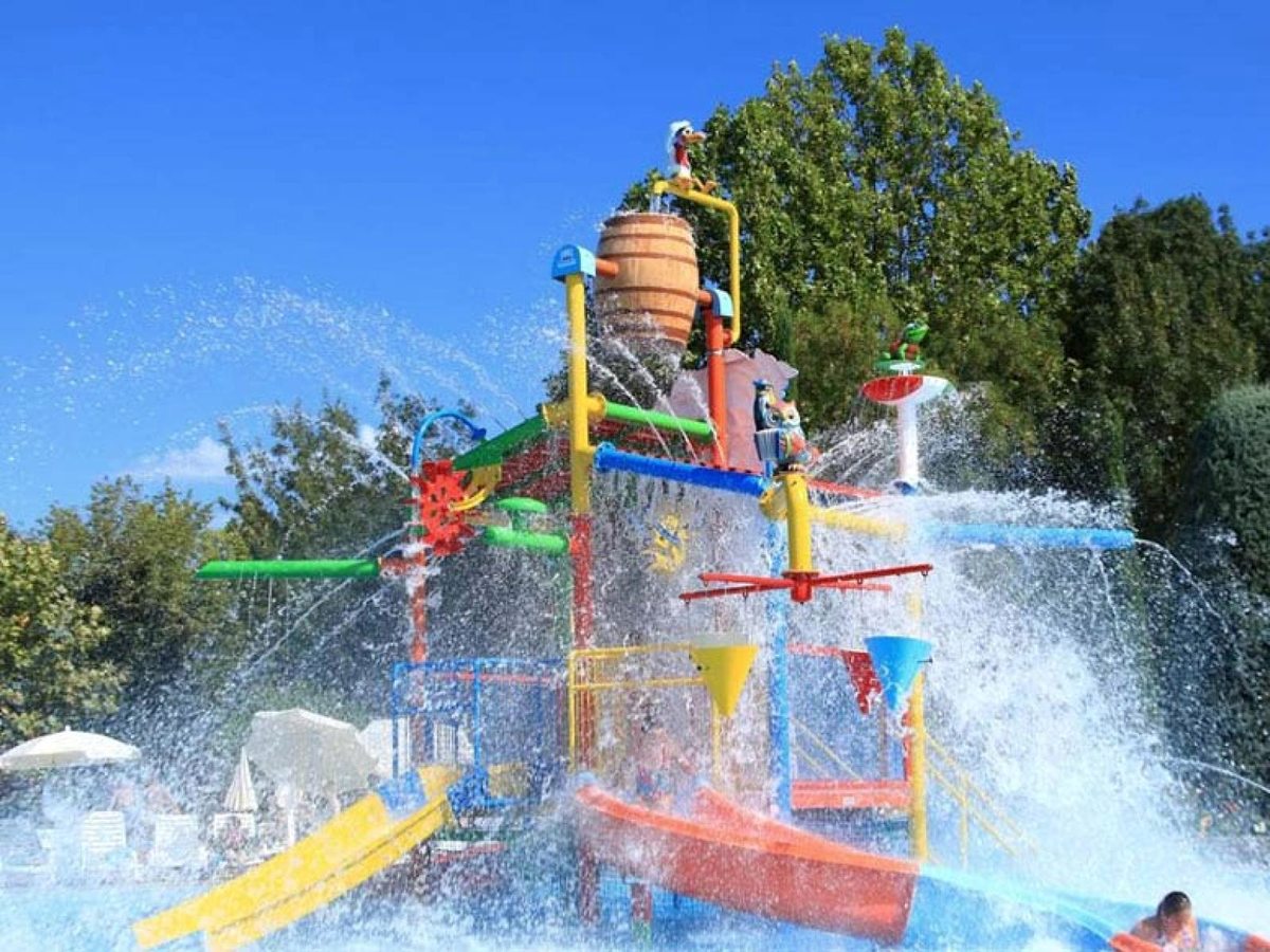 A colourful water-play tower with a tipping barrel, spray pipes and jets soaking the shallow pool below.