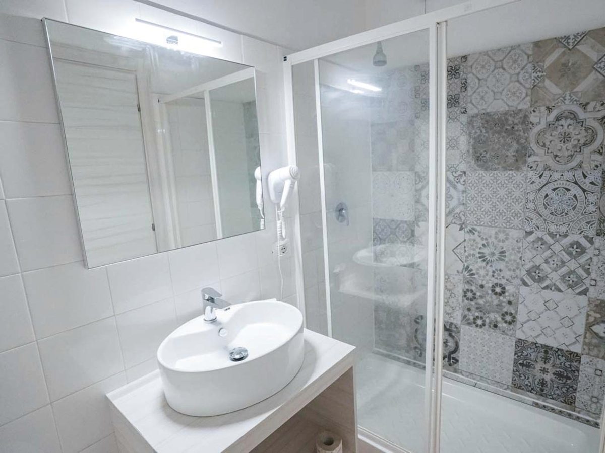 A compact bathroom with a glass walk-in shower, patterned feature tiles, a vessel basin and a large mirror.