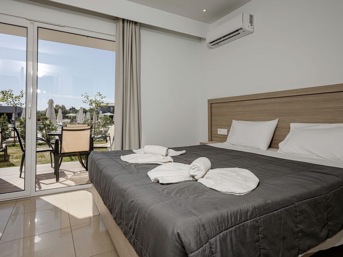 Hotel room with a double bed, air conditioning and a balcony with a table and chairs looking onto the pool and gardens.