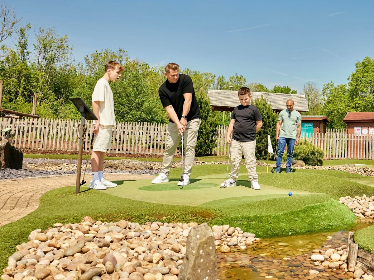 Children playing on an outdoor adventure mini-golf course with artificial greens, rock edging and a small stream.
