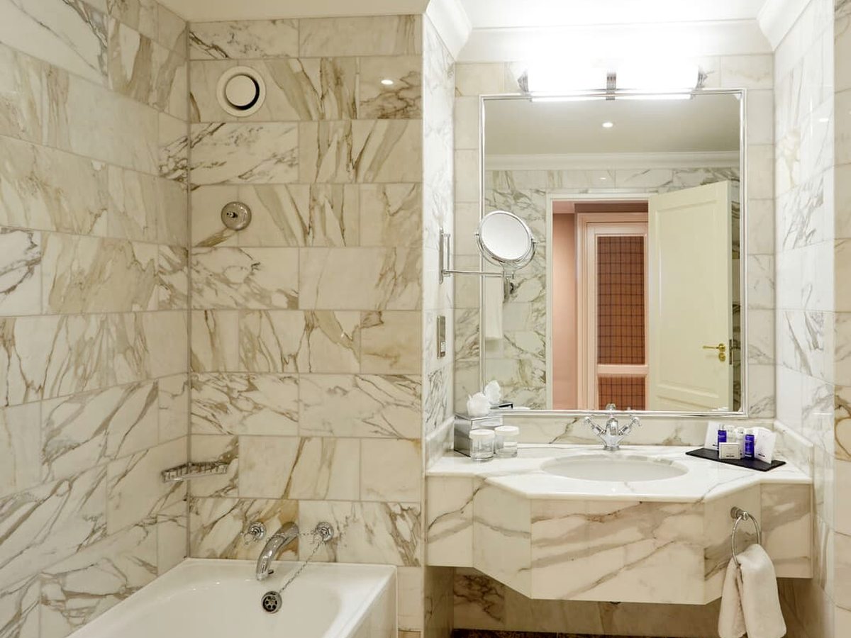 A marble-lined bathroom with a bath and shower over it, a vanity basin and a large mirror.
