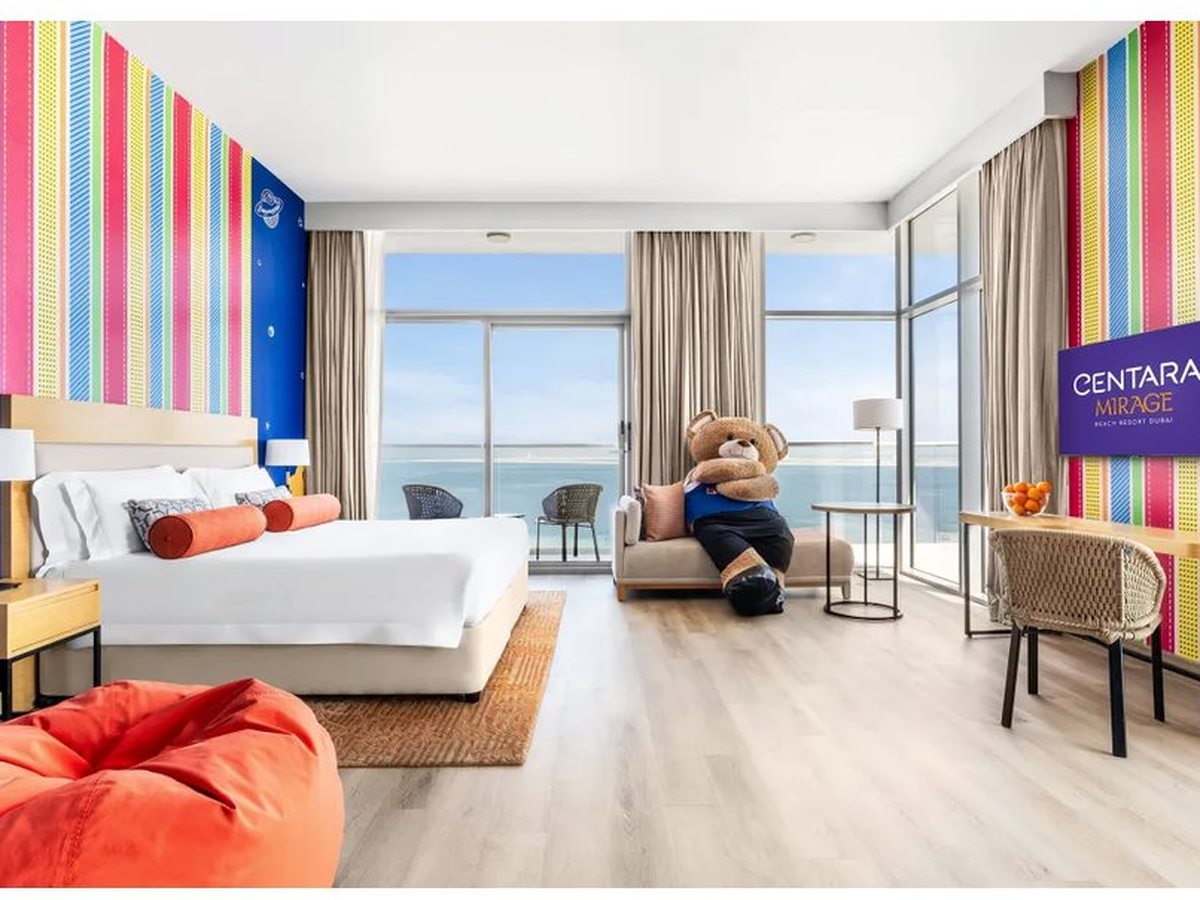 A brightly themed family room with a king bed, a rainbow-striped wall, a mural, a red beanbag and floor-to-ceiling windows onto the sea.