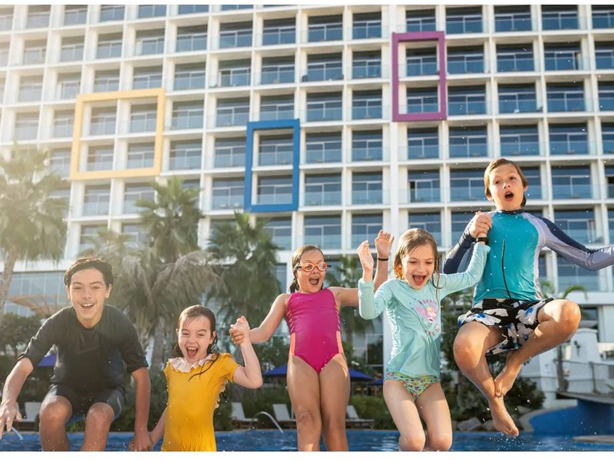 Children leaping into the large family pool, with the resort's white tower and its coloured window frames behind.