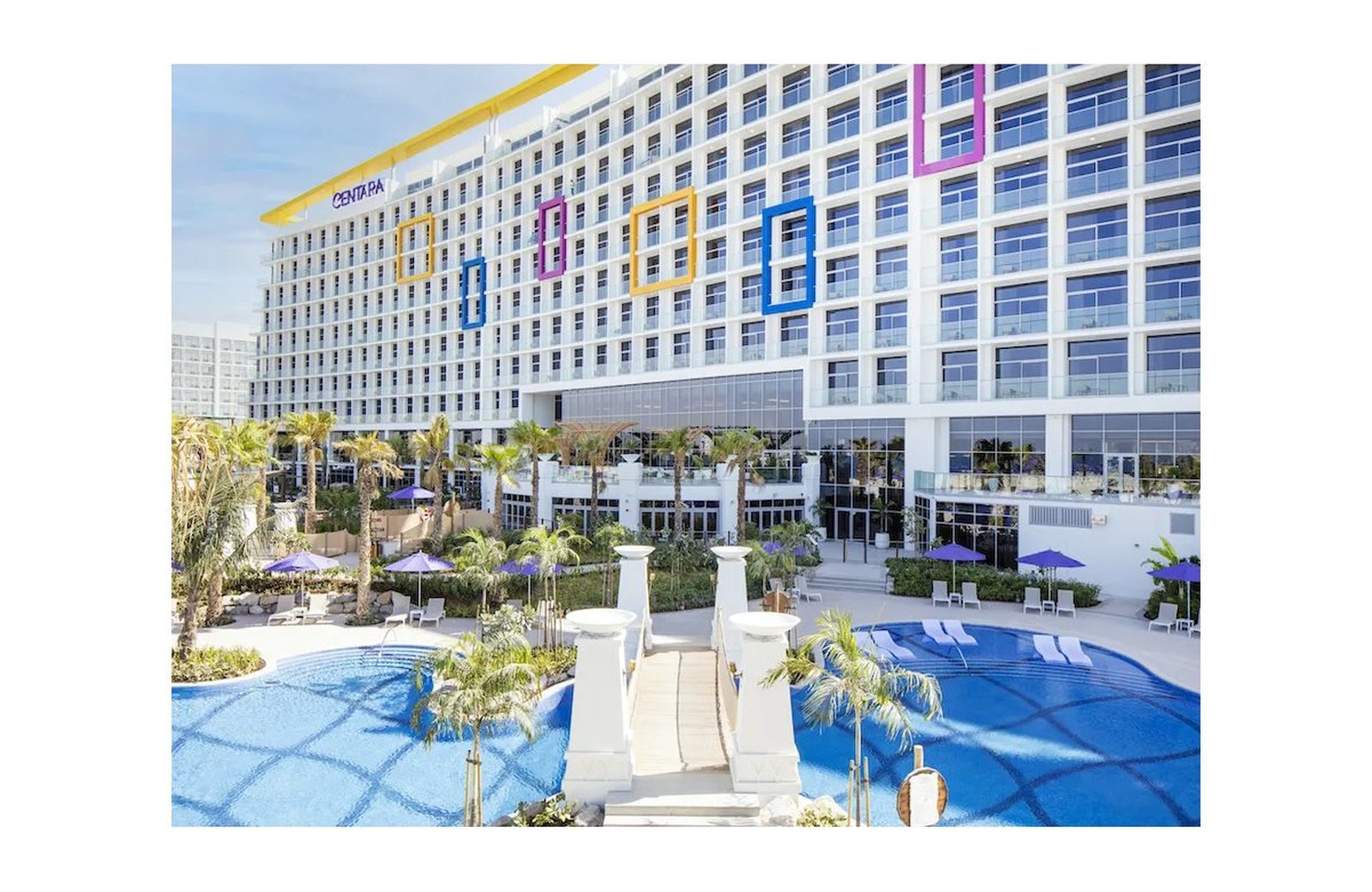 Centara Mirage Beach Resort Dubai: the white resort building with its coloured window frames, wrapped around two curved swimming pools with sun umbrellas.