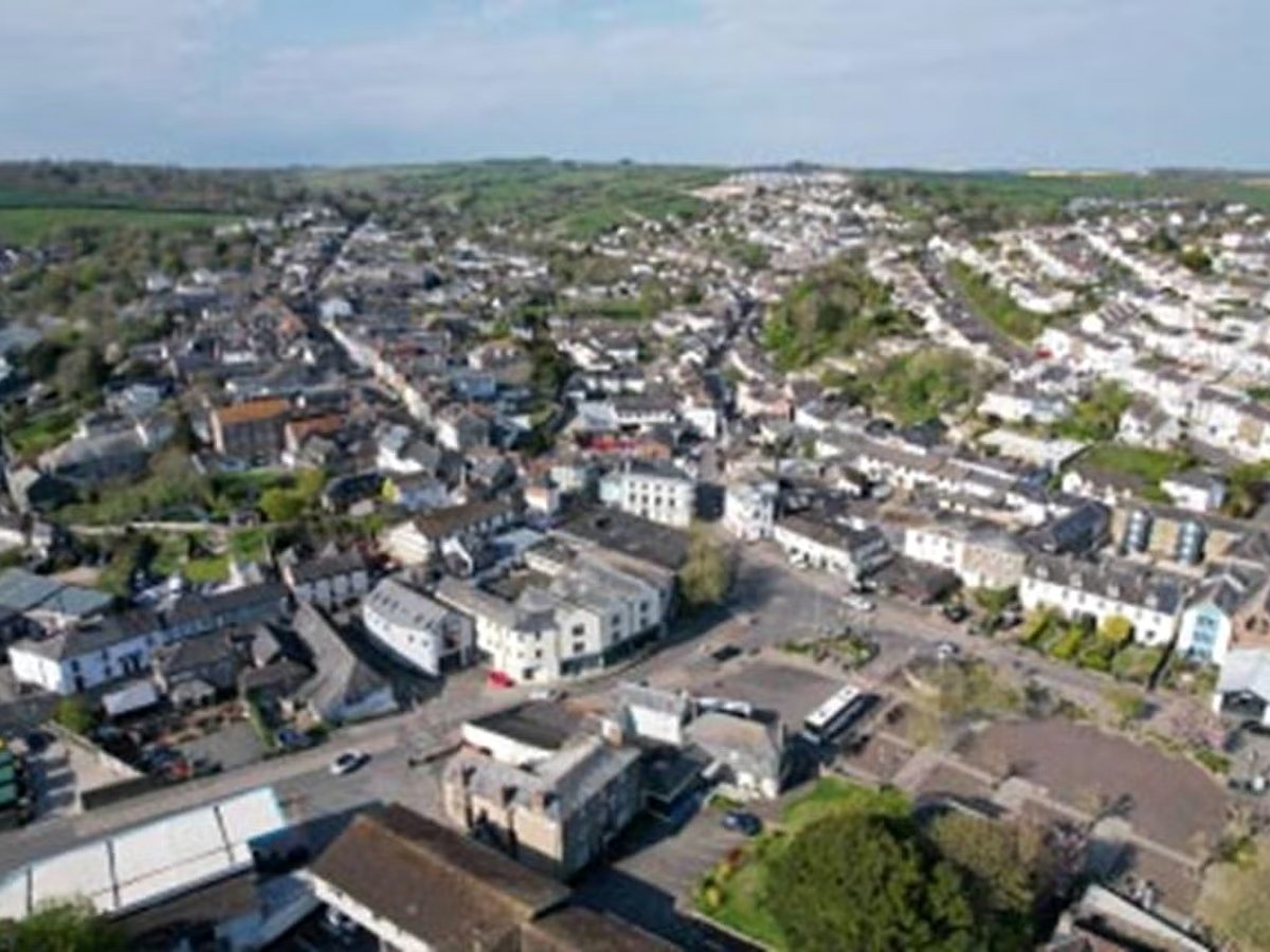 Aerial view over the packed rooftops and streets of a South Devon town set on a hillside above a river.