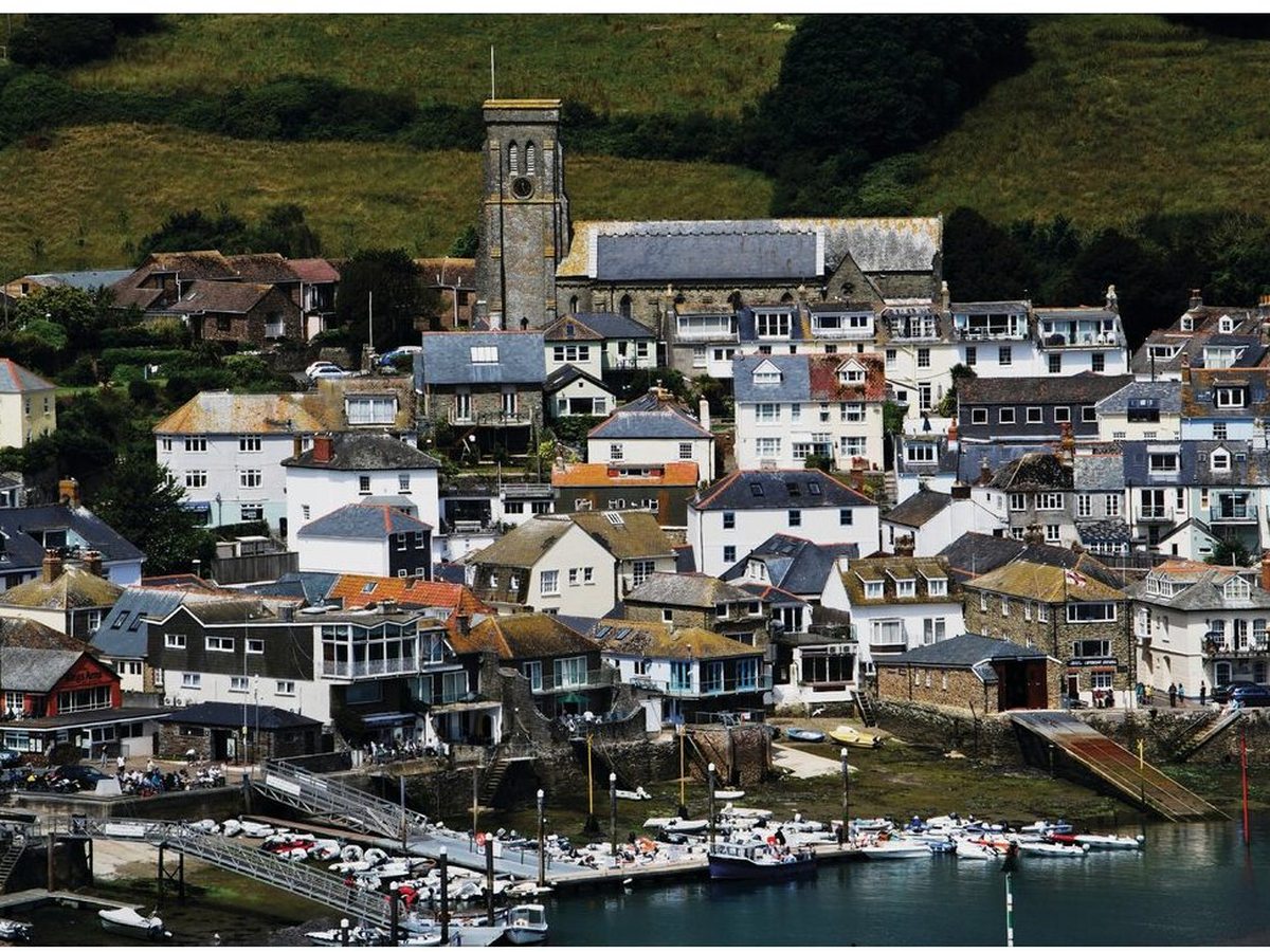 A hillside village of white and pastel houses around a small harbour, with a stone church tower rising above the rooftops and moored boats below.