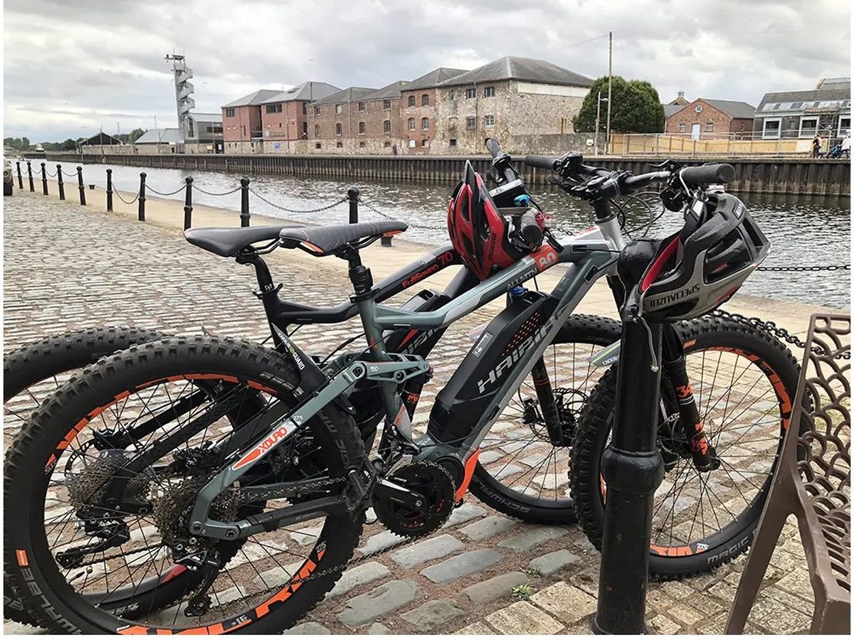 Several electric hire bikes with helmets, parked on a cobbled quayside beside the water.