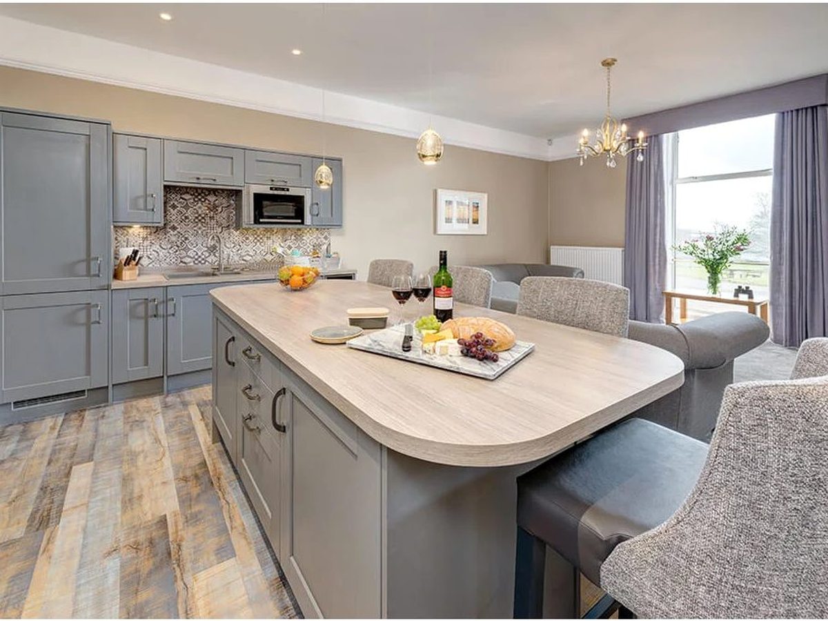 An open-plan static caravan kitchen with grey fitted units, a wood-effect worktop and a breakfast bar with high stools.