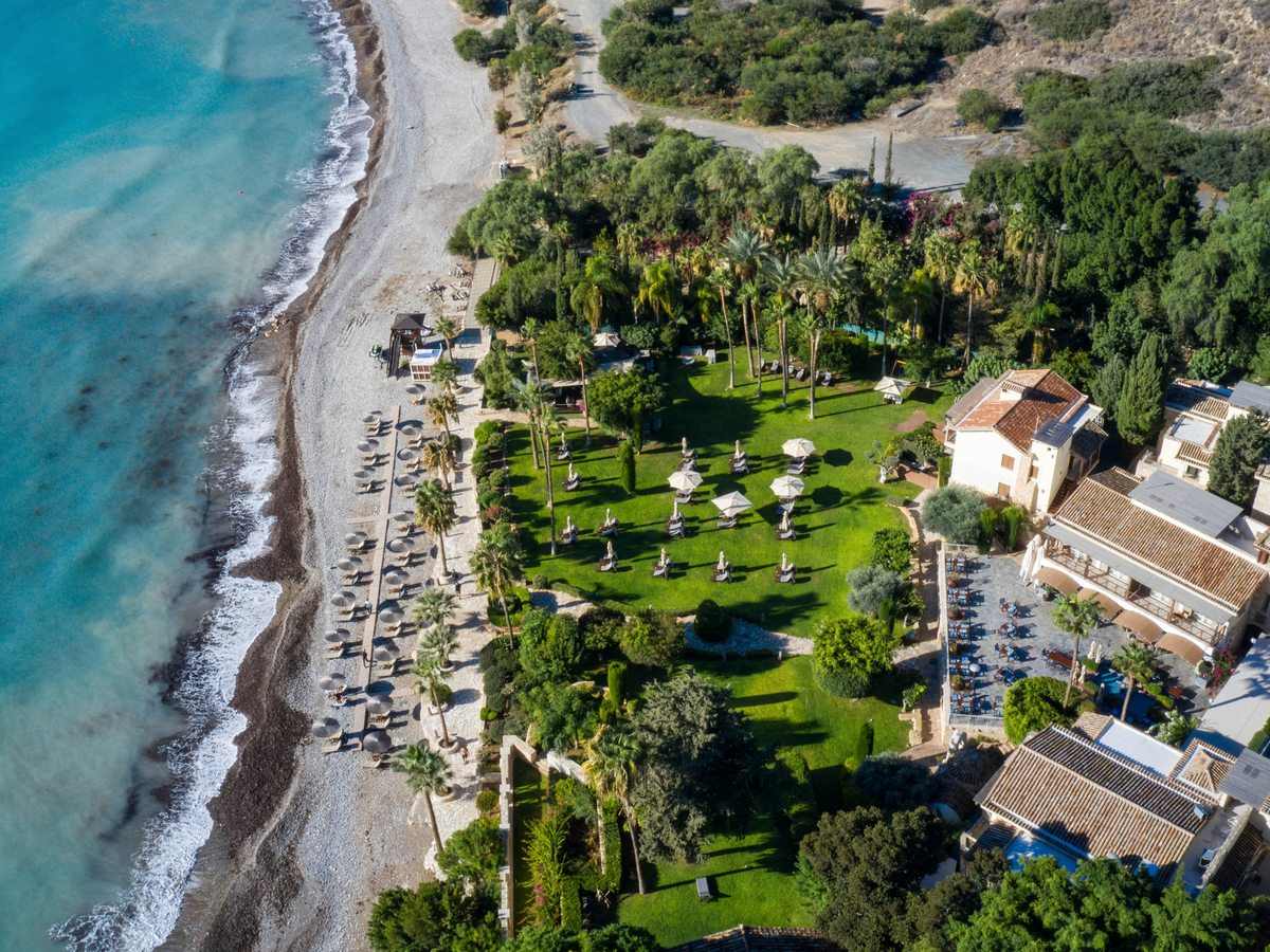 An aerial view of the shingle beach lined with parasols and sun loungers below the resort's lawns and gardens.