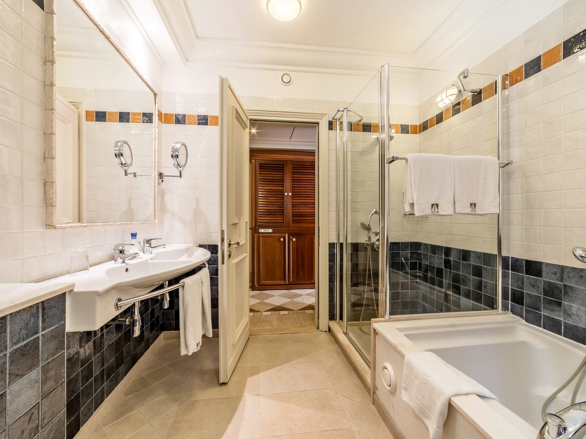 A suite bathroom with a bath, a separate glass shower cubicle, a double vanity and large mirrors.