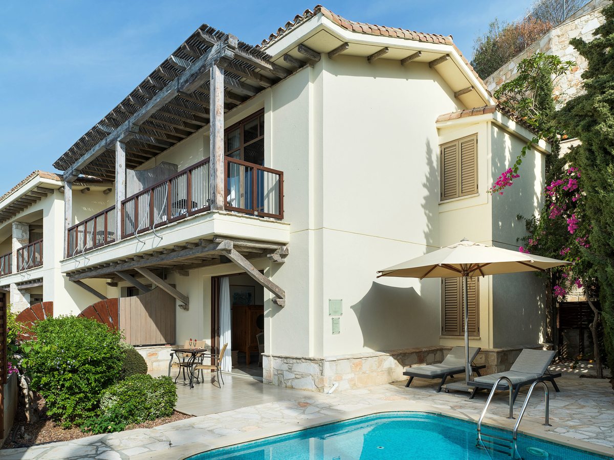 A whitewashed two-storey suite with wooden balconies, a paved terrace, a parasol, sun loungers and a small private pool.